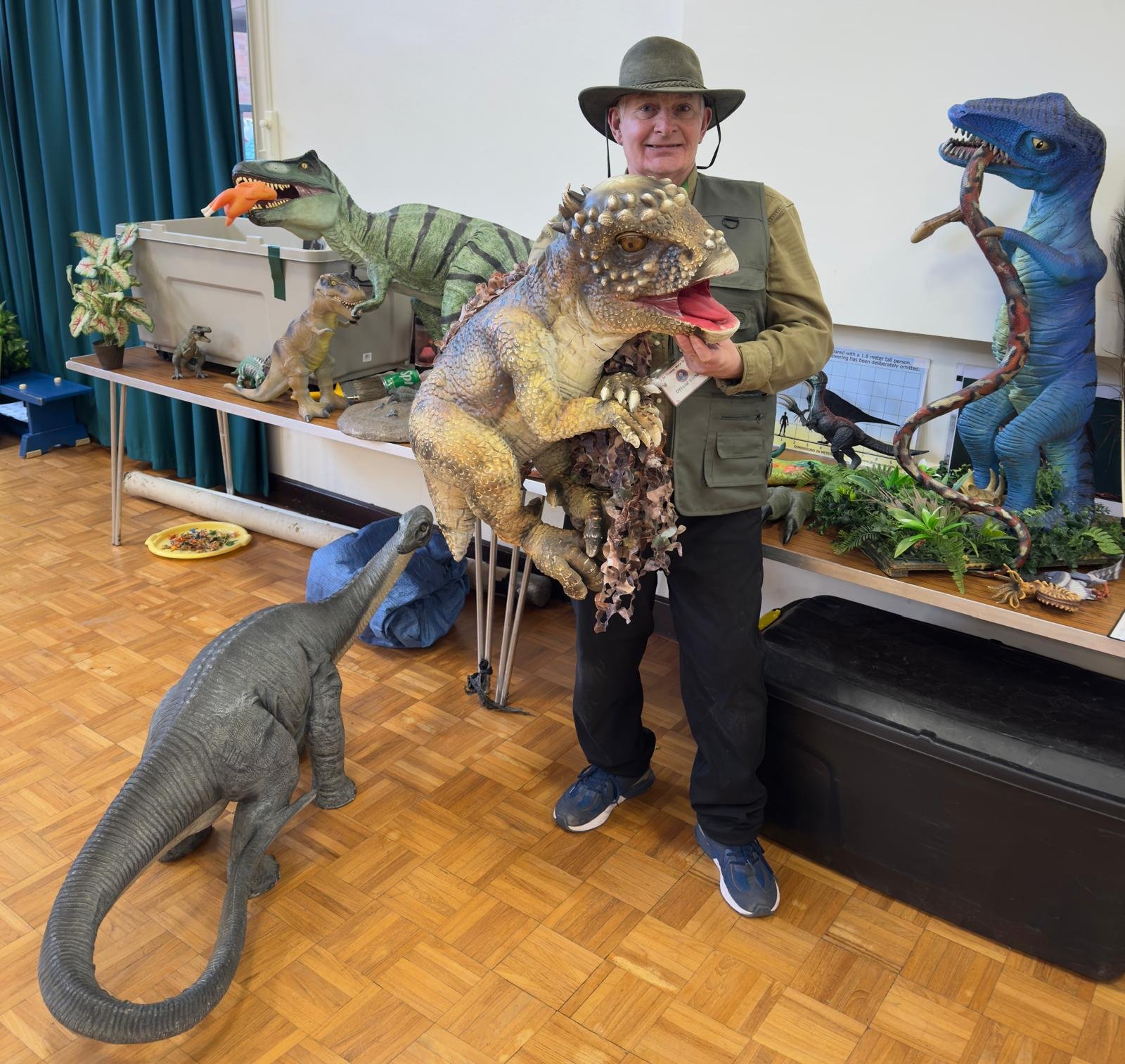 Excited presenter holding large T-Rex and Triceratops plush puppets